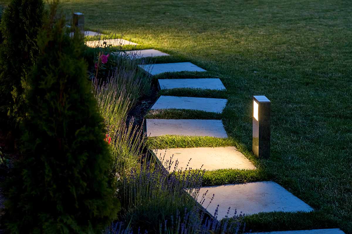 Горизонтальное изображение садовой дорожки, освещенной современными квадратными огнями ночью.